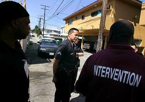TURF: Officer Robert Gimenez, center, talks with gang intervention specialists Leandre Brown, left, and Willie Pogues in the alley where Ana Interiano was killed. LAPD officers say gentrification has helped reduce crime but it hasnt pushed out gangs from their turf.
