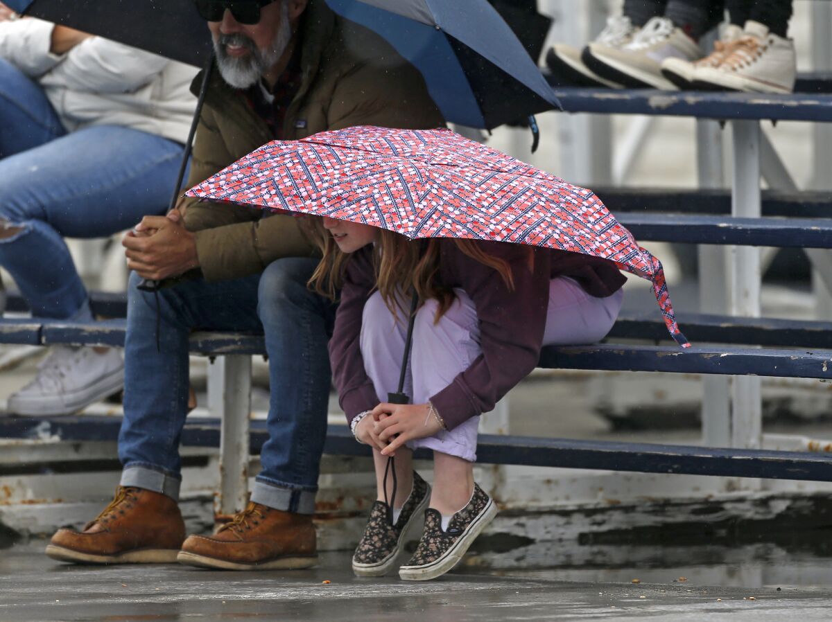 A youngster ducks under her umbrella as a heavy rain fall pounds the pool deck at Newport Harbor High.