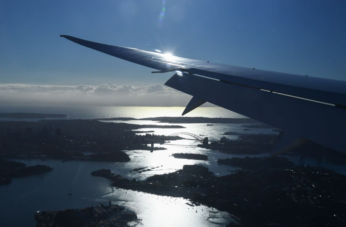 An aerial view of Sydney, including its famous bridge, and a wing as the plane approaches its landing.