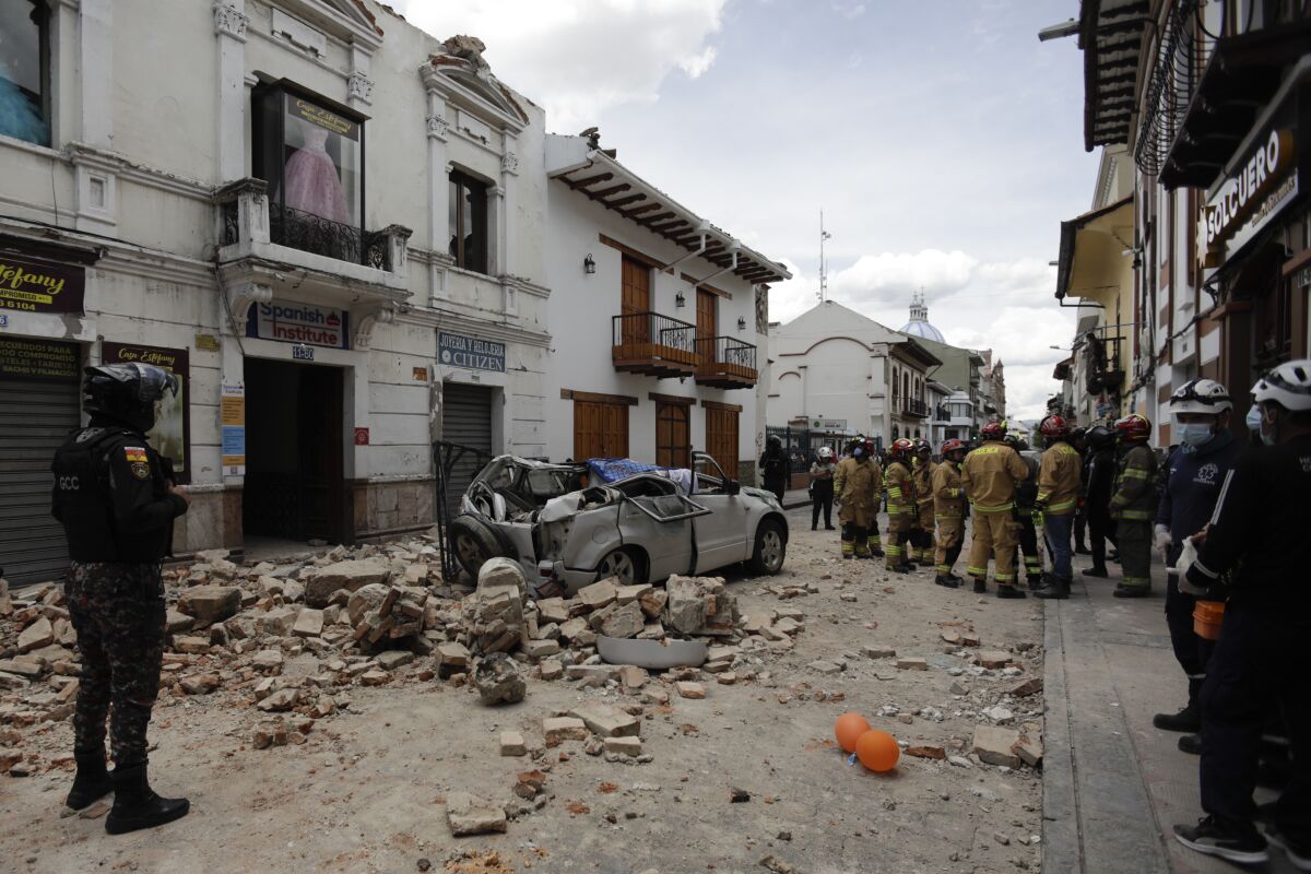 Rescue workers stand next to a car crushed by debris after an earthquake in Cuenca, Ecuador, Saturday, March 18, 2023.. The U.S. Geological Survey reported an earthquake with a magnitude of 6.7 about 50 miles south of Guayaquil. (AP Photo/Xavier Caivinagua)