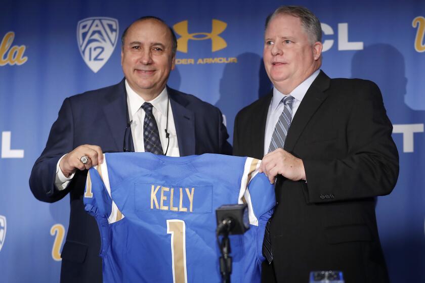 LOS ANGELES, CALIF. - NOV. 27, 2017. UCLA Athletic Director Dan Guerrero, left, and new head football coach Chip Kelly hold up a Bruins jersey with Kelly's name on it during a press conference Monday, Nov. 27, 2017, at Pauley Pavilion in Westwood. Kelly has signed a five-year, $23.9 million contract and replaces fired coach Jim Mora. (Luis Sinco/Los Angeles Times)