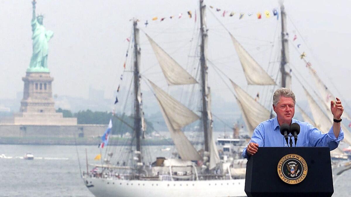 In this July 4, 2000 photo, President Clinton speaks on the USS John F. Kennedy as a tall ship passes between him and the Statue of Liberty.