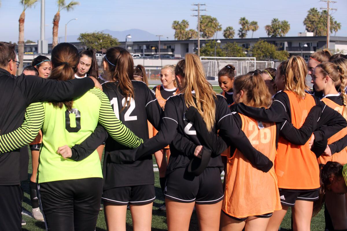 Sportswomen stand in a circle with arms linked around waists.