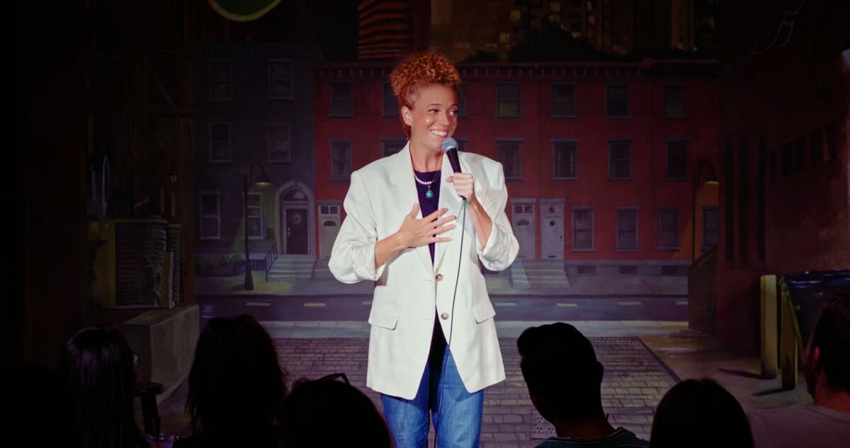 A woman standing on stage with a microphone wearing a white jacket.