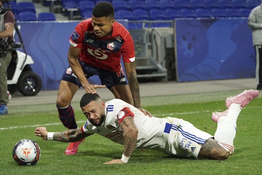Lyon's Memphis Depay, down, challenges for the ball with Lille's Reinildo Isnard Mandava, up, during their French League One soccer match in Decines, near Lyon, central France, Sunday, April 25, 2021. (AP Photo/Laurent Cipriani)