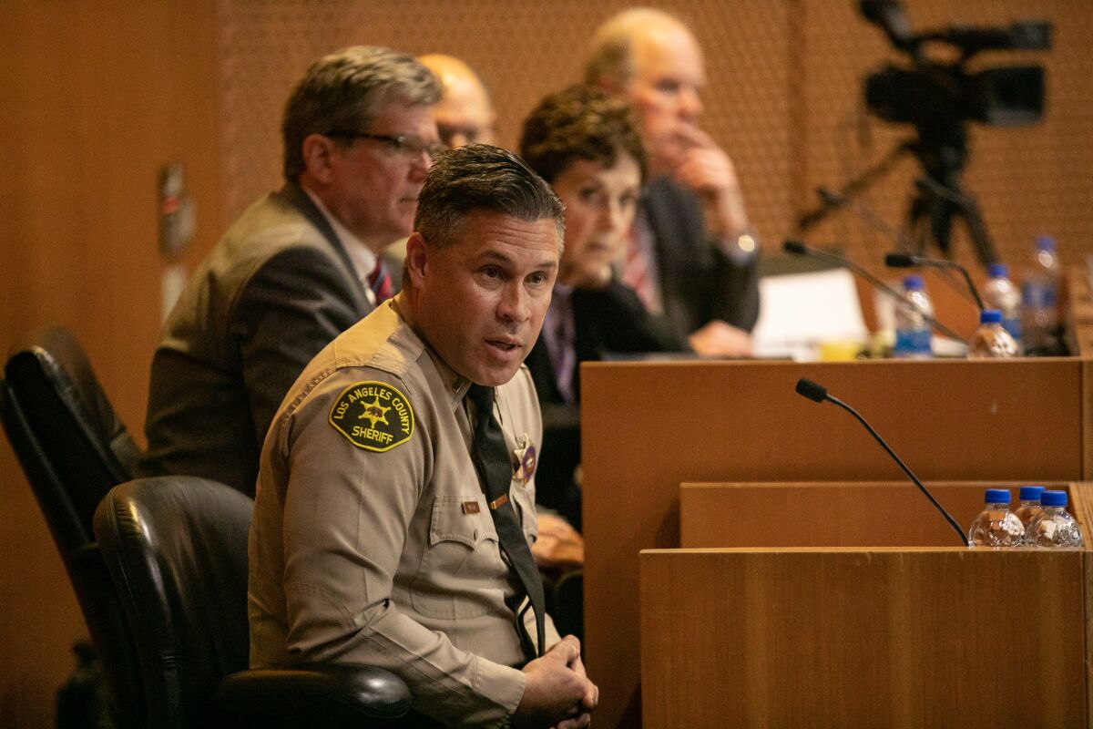 A seated law enforcement officer in uniform speaking at a microphone