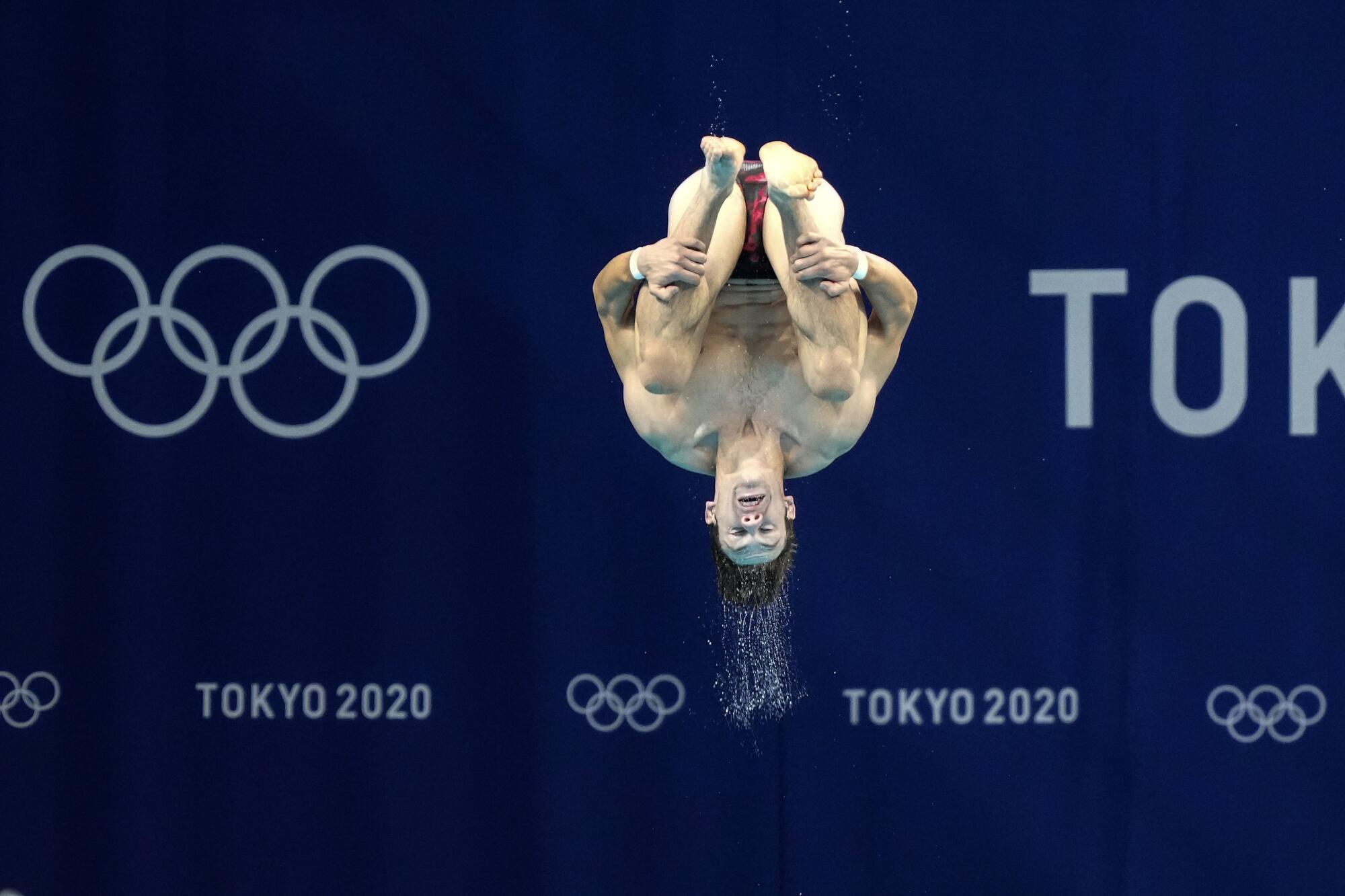 A diver jumps in front of the Olympic rings during a practice session in Tokyo.