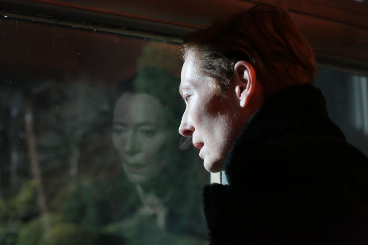 Tilda Swinton's face is reflected in a window as she leans her head against it in a scene from "The Eternal Daughter."