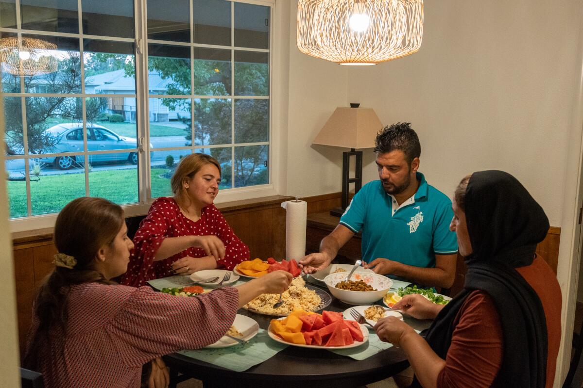 A man in a blue polo shirt is seated with three women at a table laden with food, near a window