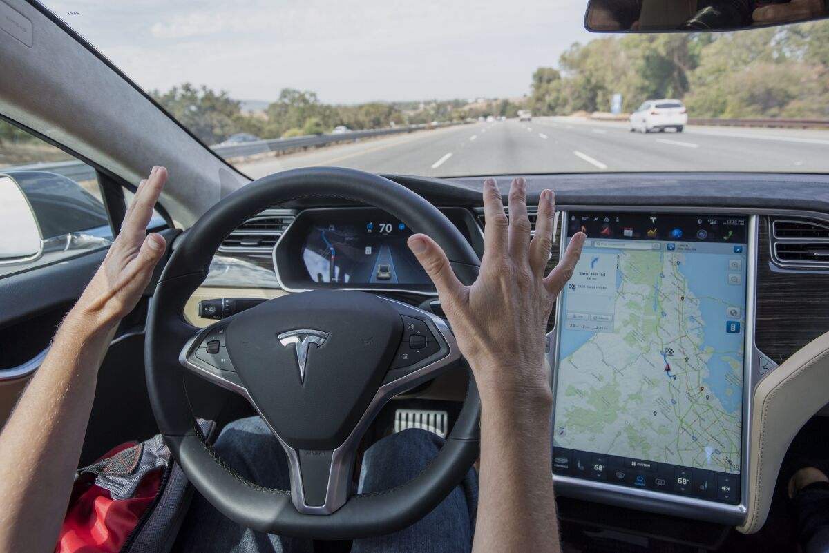 A person suspends hands over a Tesla steering wheel in self-driving mode
