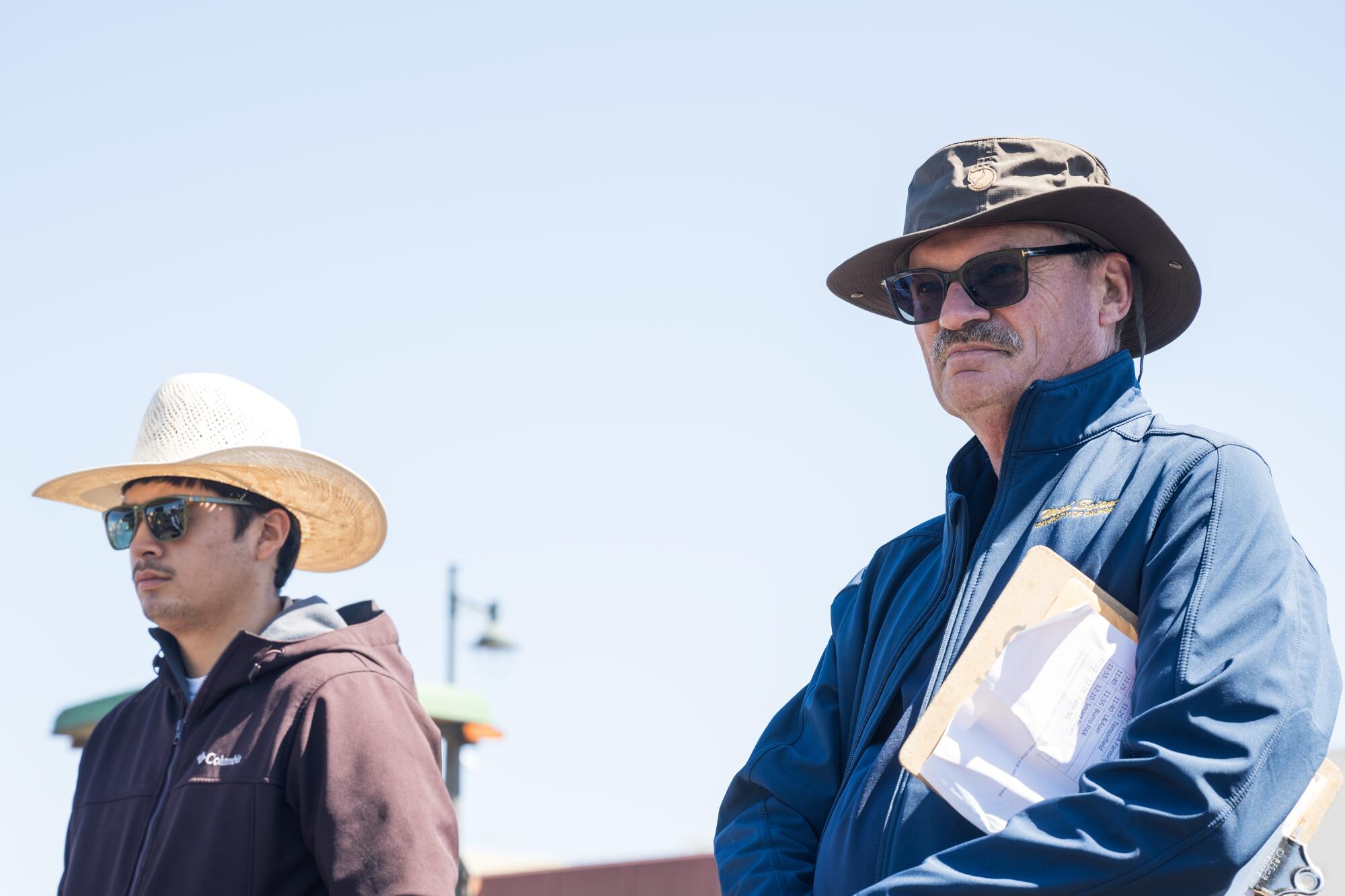 Two men in the field with sunglasses, jackets and sun hats