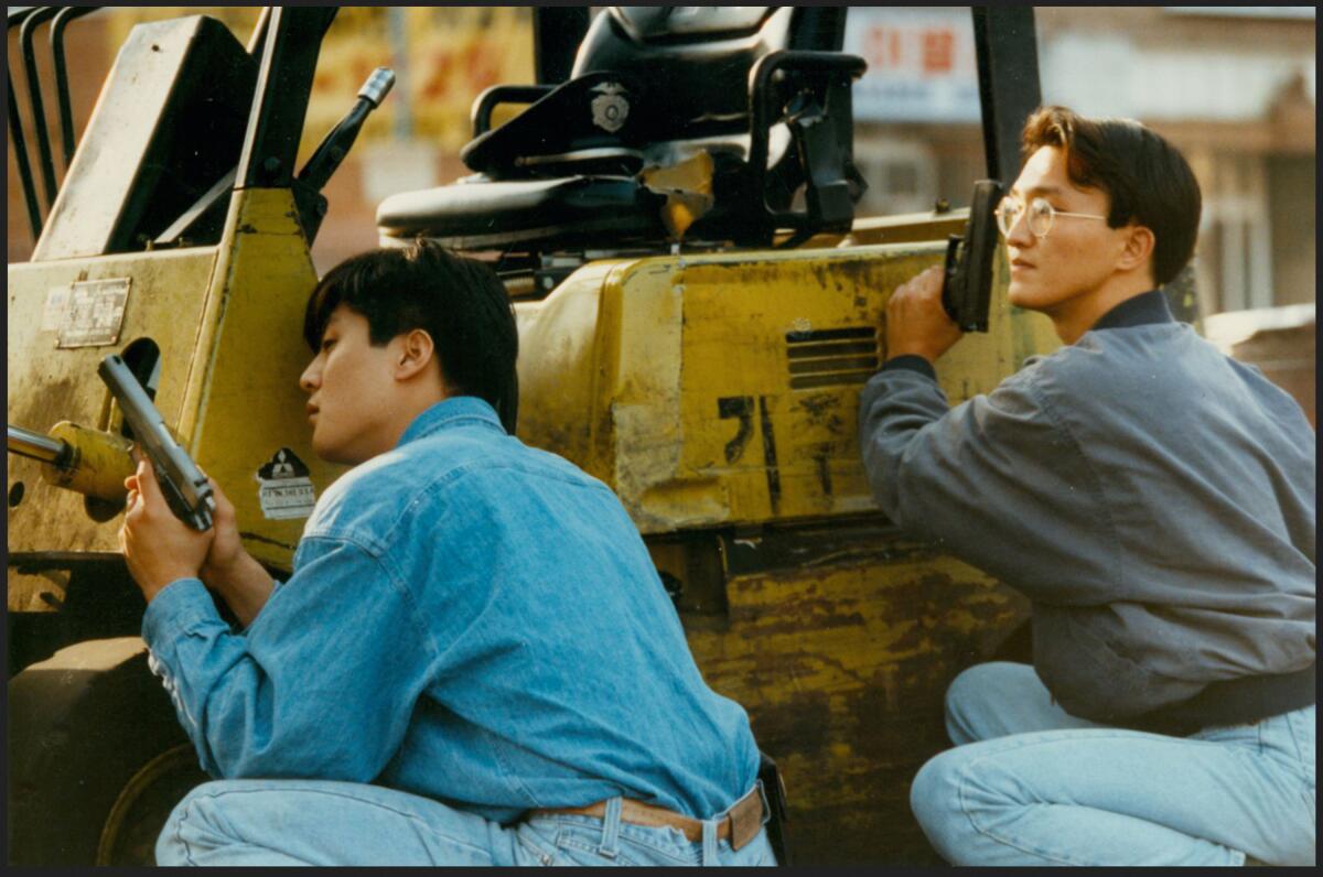 Two young men peer down a street as they hold handguns.