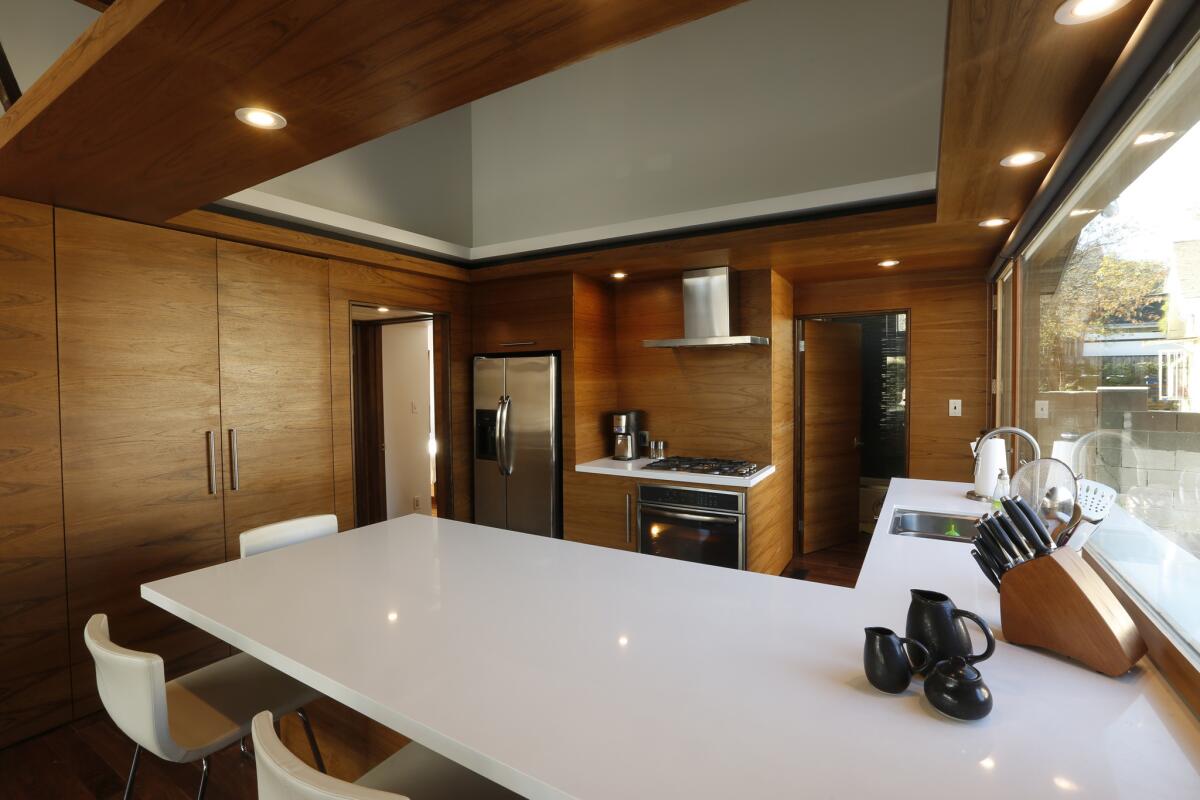 The kitchen today features inexpensive IKEA cabinets covered with teak veneer that continues onto the walls, as well as the bathroom door. A window over the kitchen counter, right, was conceived as a sliding door turned on its side.