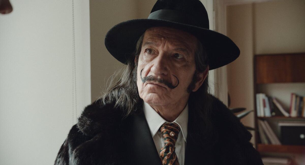 A man with a curled mustache in a jacket and tie and black hat