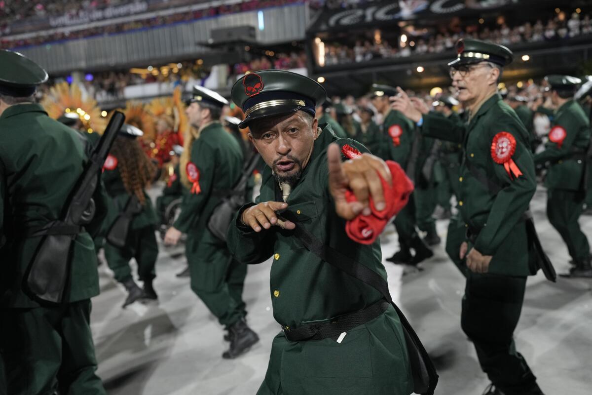 Performers in green uniforms with a red ribbon on each one parade during Carnival celebrations.