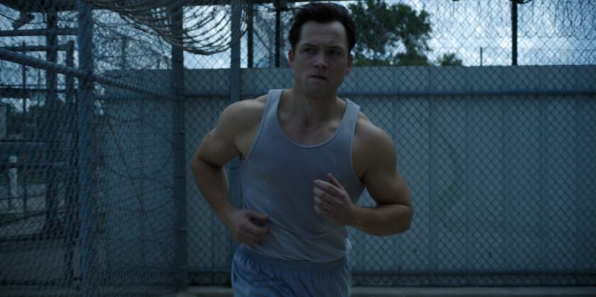 A man in a gray tank top works out in a prison yard