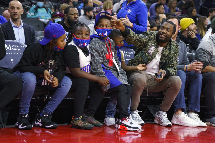 Rapper Meek Mill, right, sits courtside children from families that have been adversely affected by the criminal justice system during the first half of an NBA basketball game the Miami Heat and the Philadelphia 76ers, Wednesday, Dec. 15, 2021, in Philadelphia. (AP Photo/Chris Szagola)