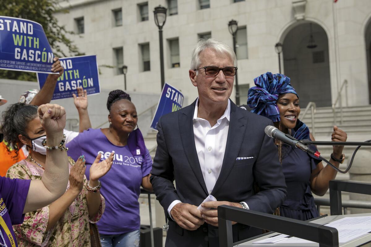 A person at a lectern outside, with people cheering behind him.