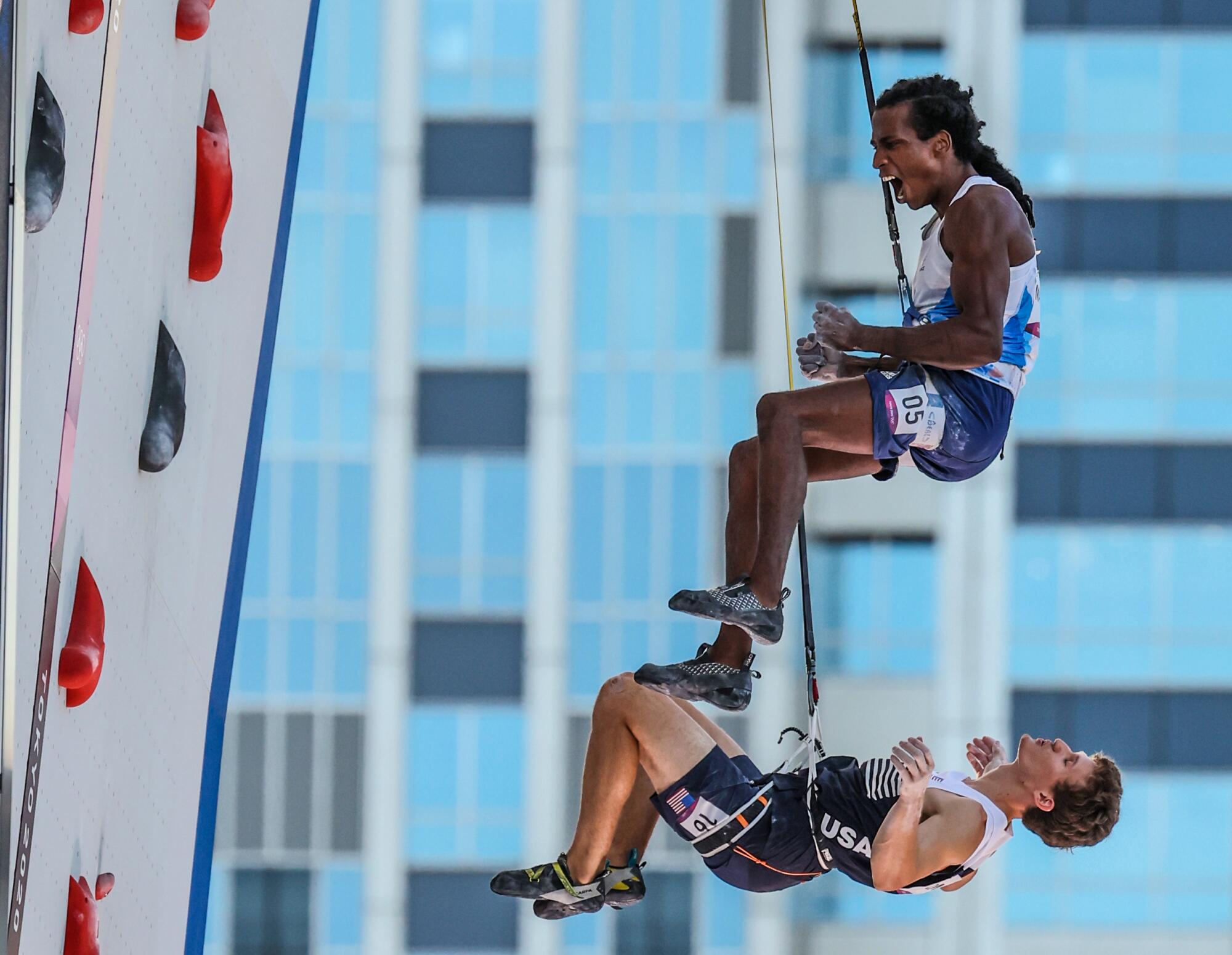 Mickael Mawem and Nathaniel Coleman are suspended by ropes next to a climbing wall.