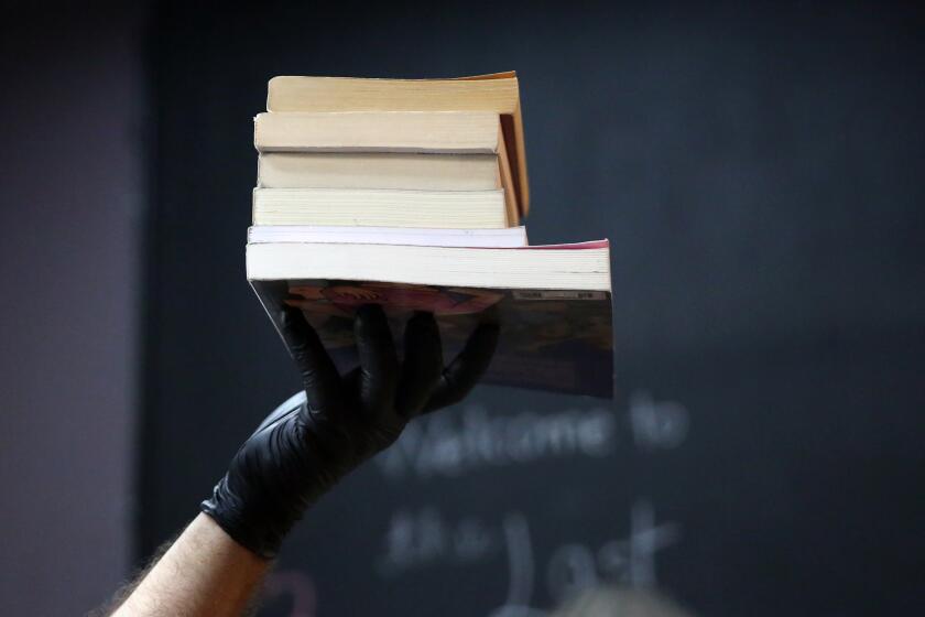 LOS ANGELES, CA - MAY 18: Eric Larkin holds up a stack of books for a picture to send to a customer to confirm the order is okay in The Last Bookstore on Monday, May 18, 2020 in Los Angeles, CA. The Last Bookstore in downtown Los Angeles is among the stores that have decided to reopen for curbside pickups where customers can pull into a designated spot, call a number and have their orders handed over. (Dania Maxwell / Los Angeles Times)