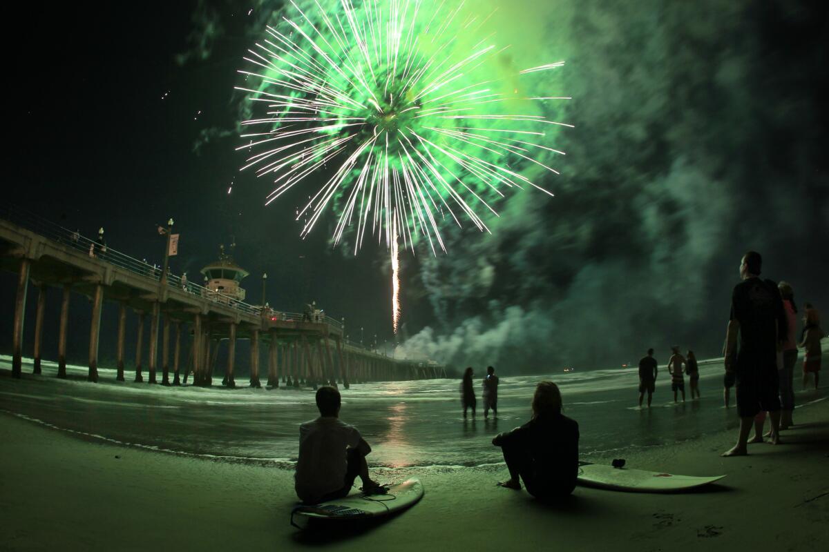 Surfers Breden Salstrom, left, and Omar Haddad, both of Huntington Beach, watch as fireworks launch from the Huntington Beach pier on the Fourth of July in 2014.