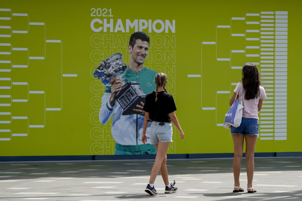 Visitors stop to take a photo of a billboard featuring defending champion Serbia's Novak Djokovic ahead of the Australian Open at Melbourne Park in Melbourne, Australia, Tuesday, Jan. 11, 2022. The prime ministers of Australia and Serbia have discussed Novak Djokovic's precarious visa after the top-ranked Serbian tennis star won a court battle to compete in the Australian Open but still faces the threat of deportation because he is not vaccinated against COVID-19. (AP Photo/Mark Baker)