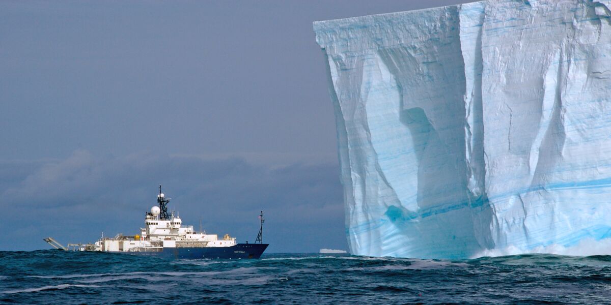 The Scripps Institution of Oceanography research vessel Roger Revelle cruises past an iceberg in the Antarctic.