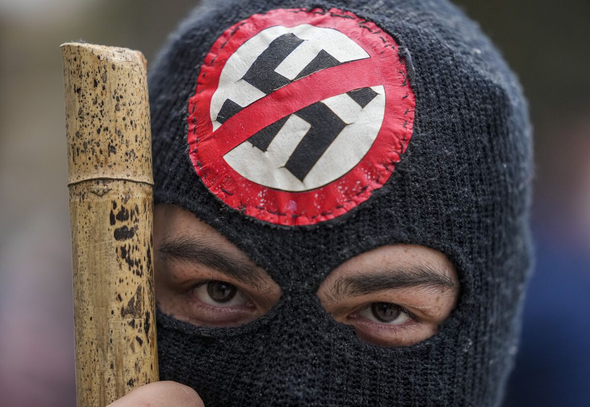 A protester wears a mask adorned with an anti-Nazi symbol during protests marking the 48th anniversary of the 1973 military coup and the death of Chile's late President Salvador Allende, in Santiago, Chile, Saturday, Sept. 11, 2021. The coup ousting the democratically elected leader, Allende, began the dictatorship of Gen. Augusto Pinochet. (AP Photo/Esteban Felix)