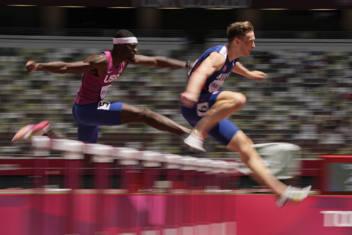 Norway's Karsten Warholm leads Rai Benjamin of the United States while leaping a hurdle.