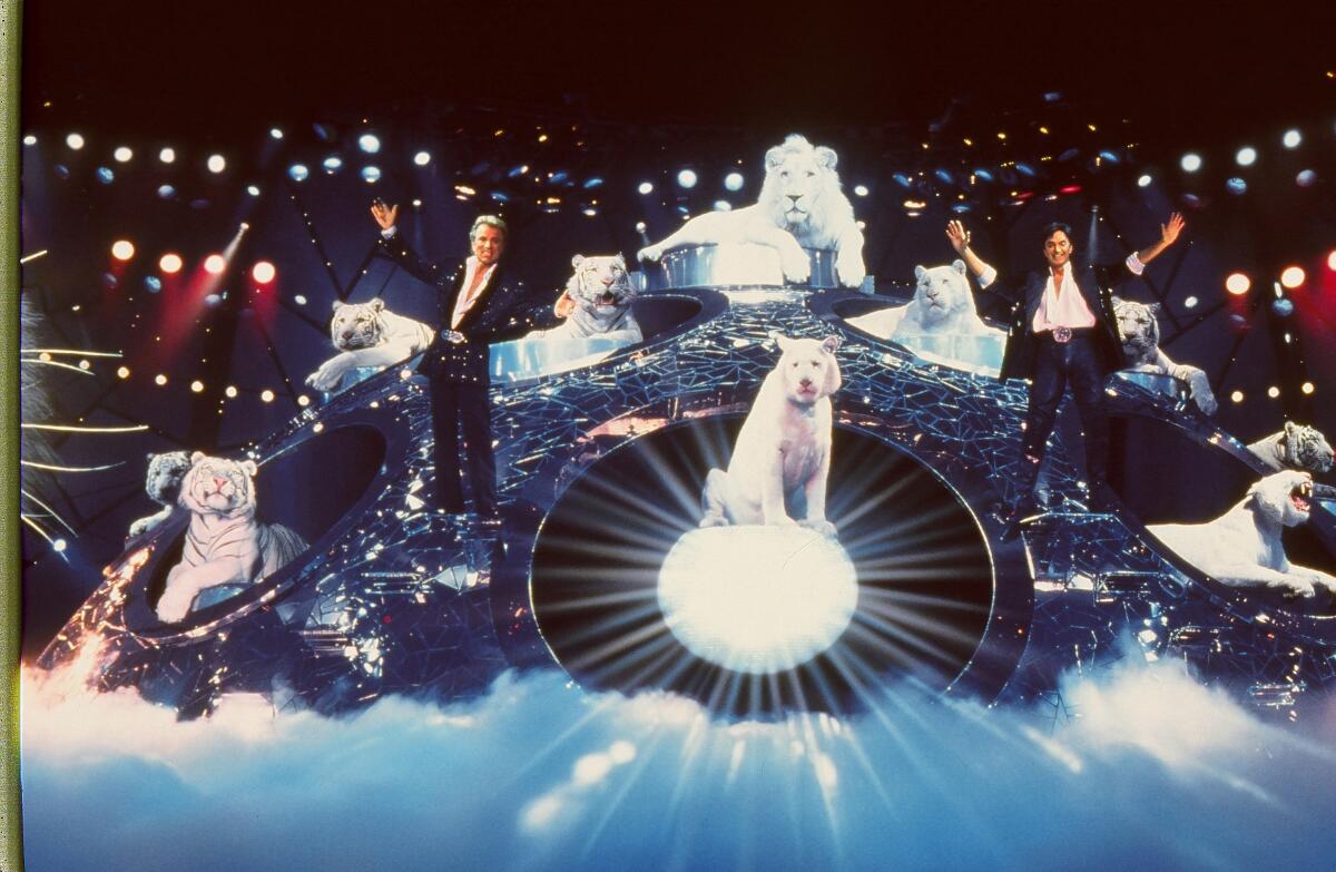 Two men, flanked by white tigers, pose on an elaborate stage.