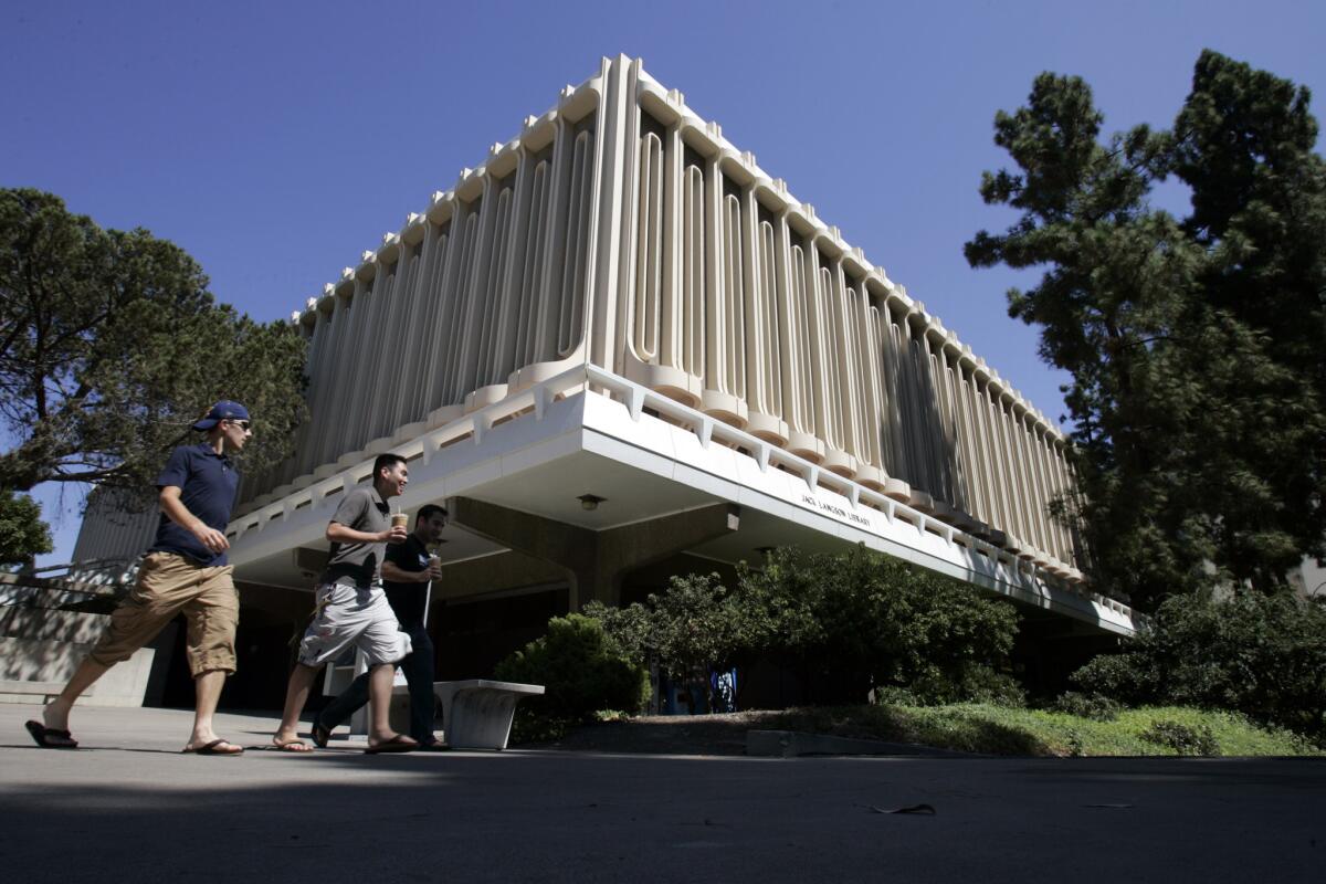People walk through the University of California, Irvine campus past the Jack Langson Library.