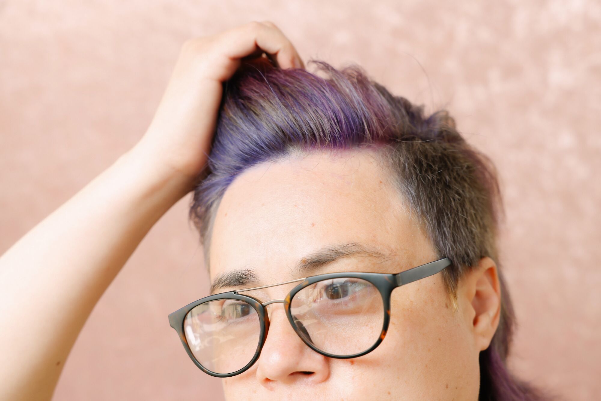 A woman with purple hair and glasses runs her fingers through her hair.