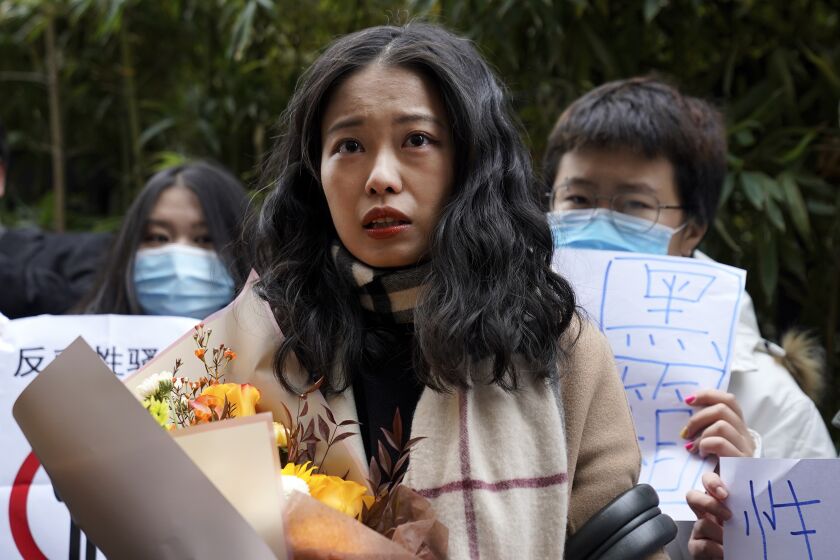 Zhou Xiaoxuan, center, speaks to her supporters holding banners as she arrives at a courthouse in Beijing, Wednesday, Dec. 2, 2020. Zhou, a Chinese woman who filed a sexual harassment lawsuit against a TV host, told dozens of cheering supporters at a courthouse Wednesday she hopes her case will encourage other victims of gender violence in a system that gives them few options to pursue complaints.(AP Photo/Andy Wong)
