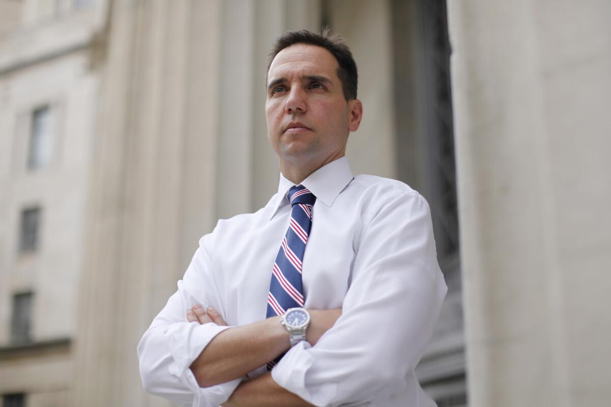 A man in shirt and tie stands with arms folded 