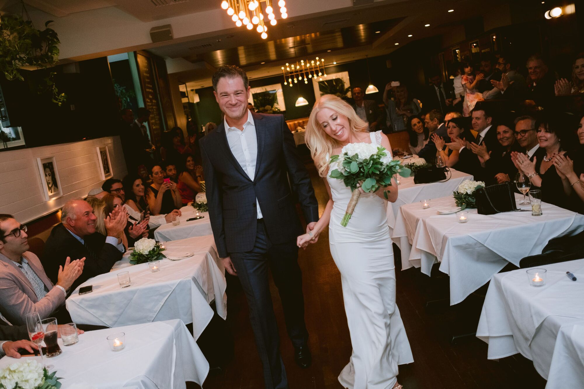 Jonah Keri and Amy Kaufman walk between an aisle of table on their wedding day