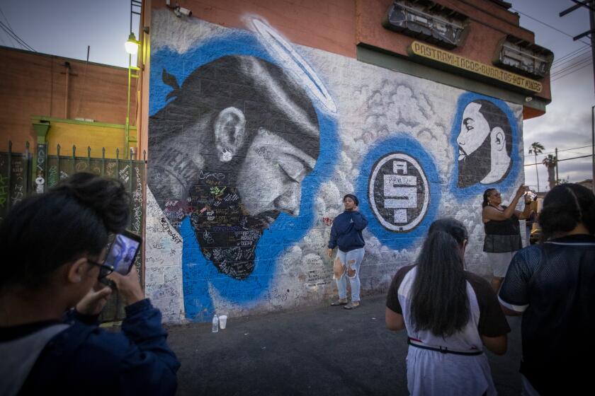 LOS ANGELES, CALIF. -- THURSDAY, JULY 18, 2019: Tourists and visitors take photos and video with Nipsey Hussle murals at the strip mall property owned by Nipsey Hussle in South Los Angeles, which has seen a steady flow of tourists and heightened police presence in light of recent trouble and gang presence. The strip mall includes HussleÕs Marathon Clothing store, as well as other businesses. Photo taken in Los Angeles, Calif., on July 18, 2019. (Allen J. Schaben / Los Angeles Times)