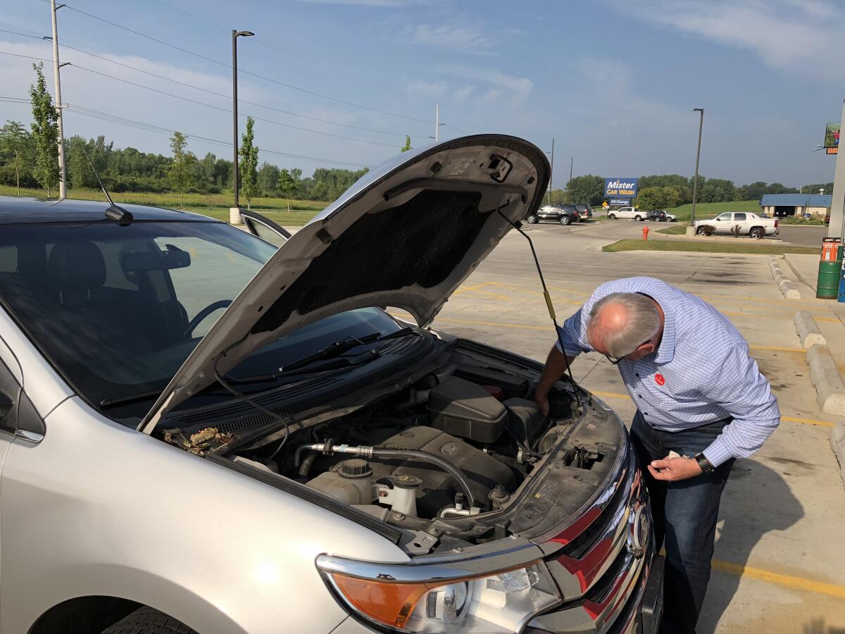 Tim Walz reaches into the engine of a new vehicle with the hood open