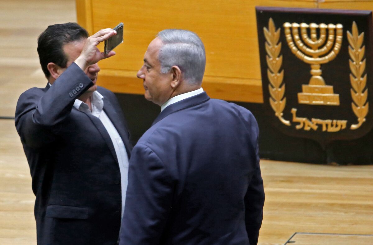 Ayman Odeh, left, leader of the Joint List of Arab parties in Israel’s parliament, uses a phone to take a close-up picture of Prime Minister Benjamin Netanyahu in the Knesset chamber in Jerusalem on Sept. 11, 2019. Netanyahu and Odeh clashed during a discussion before a vote on a controversial bill to allow cameras in polling booths.