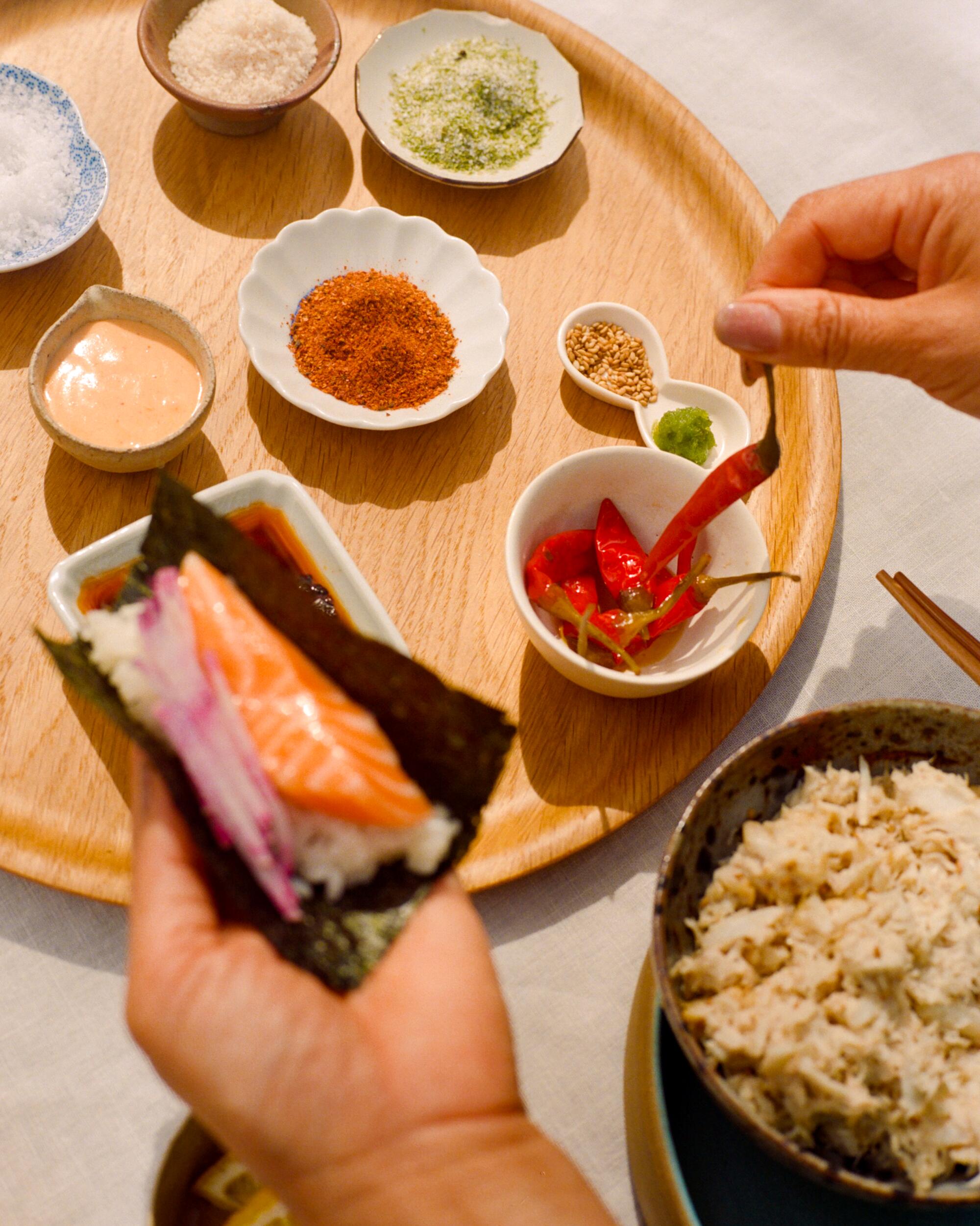 One hand holds a hand roll while the other hand loads up on condiments.