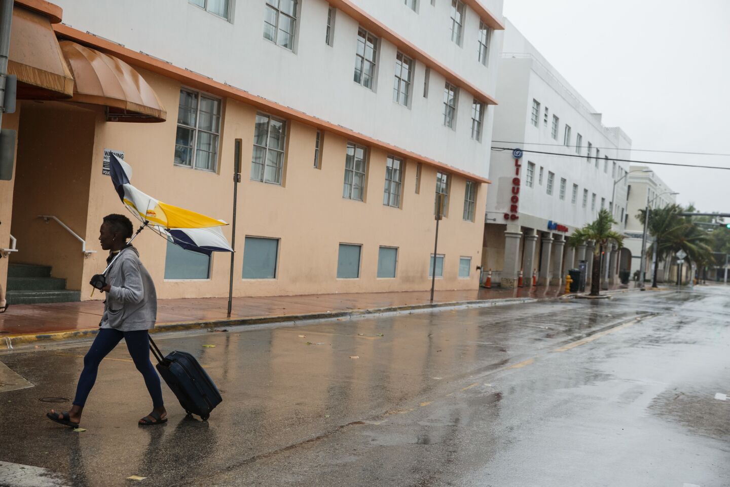 Abby Jenkins walks against the wind with her luggage and umbrella to get to safety, in Miami Beach.