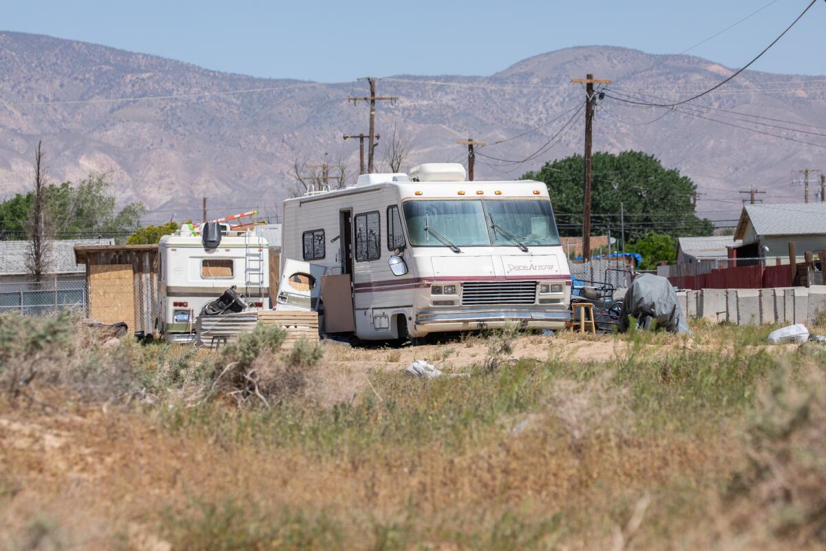 RVs on a dirt lot with weeds in a desert area near mountains