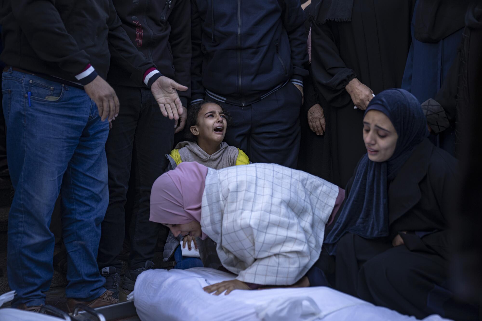 Palestinian women and a child weep next to a shrouded body.