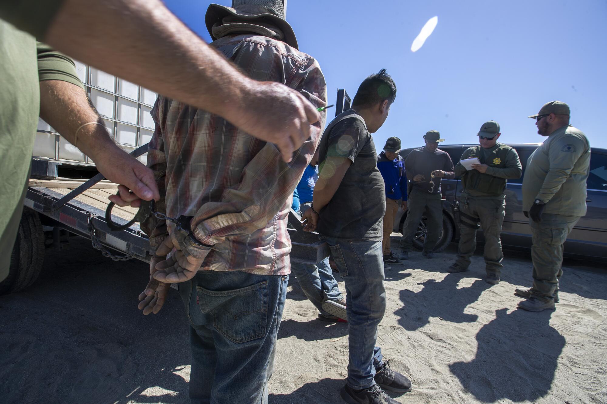 Sheriff's deputies interview handcuffed workers while serving a search warrant.