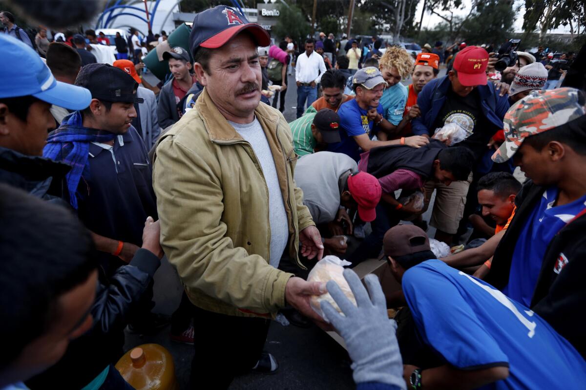 Immigrants who are part of a migrant caravan that has made its way from Honduras swarm around a man handing out food outside the Benito Juarez Sports Center in Tijuana.