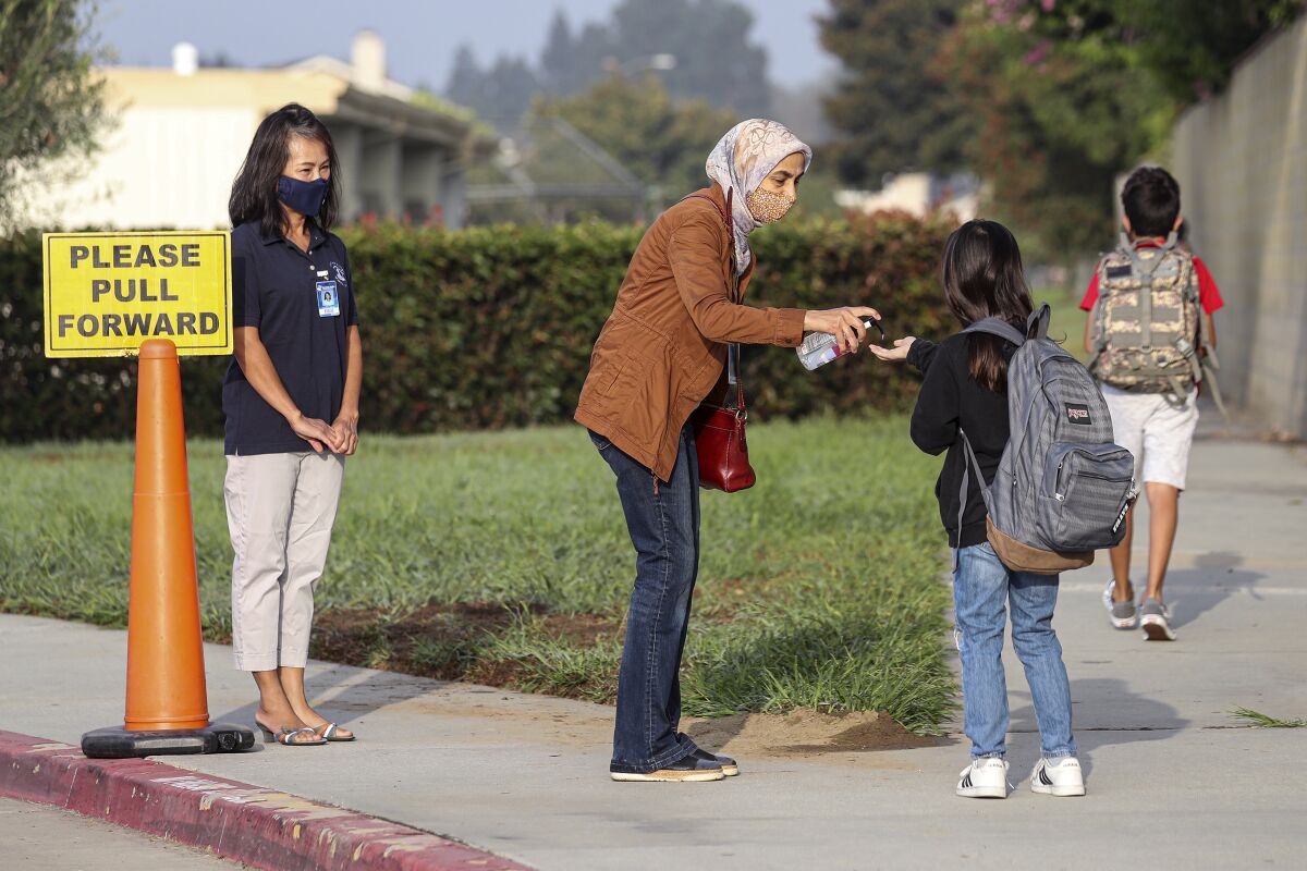 A woman squirts sanitizer into the waiting hand of a student outside school