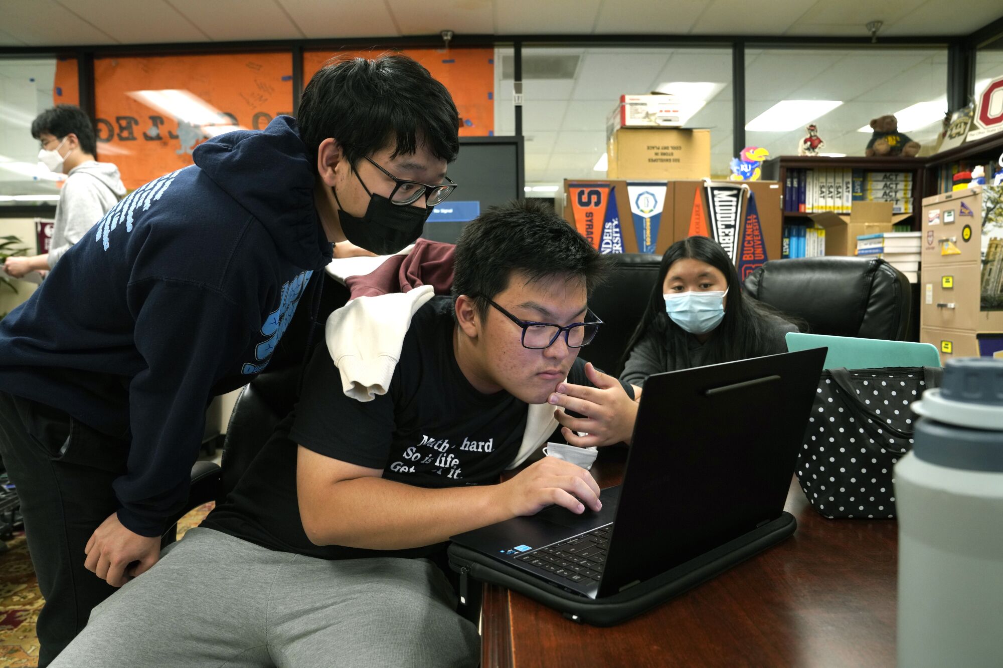 Three students huddle around a laptop in a room
