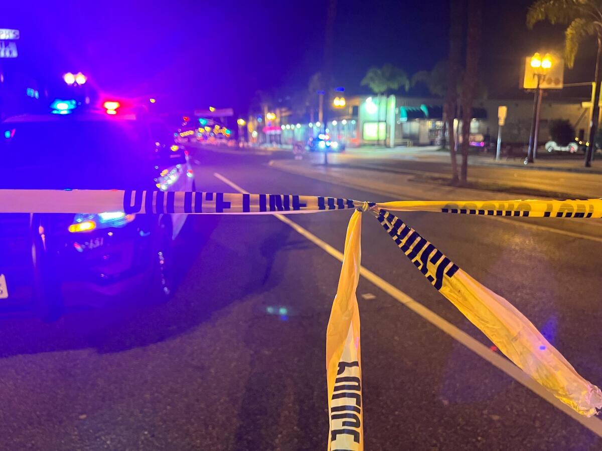 A police car, lights flashing, is seen on a street behind yellow police tape 