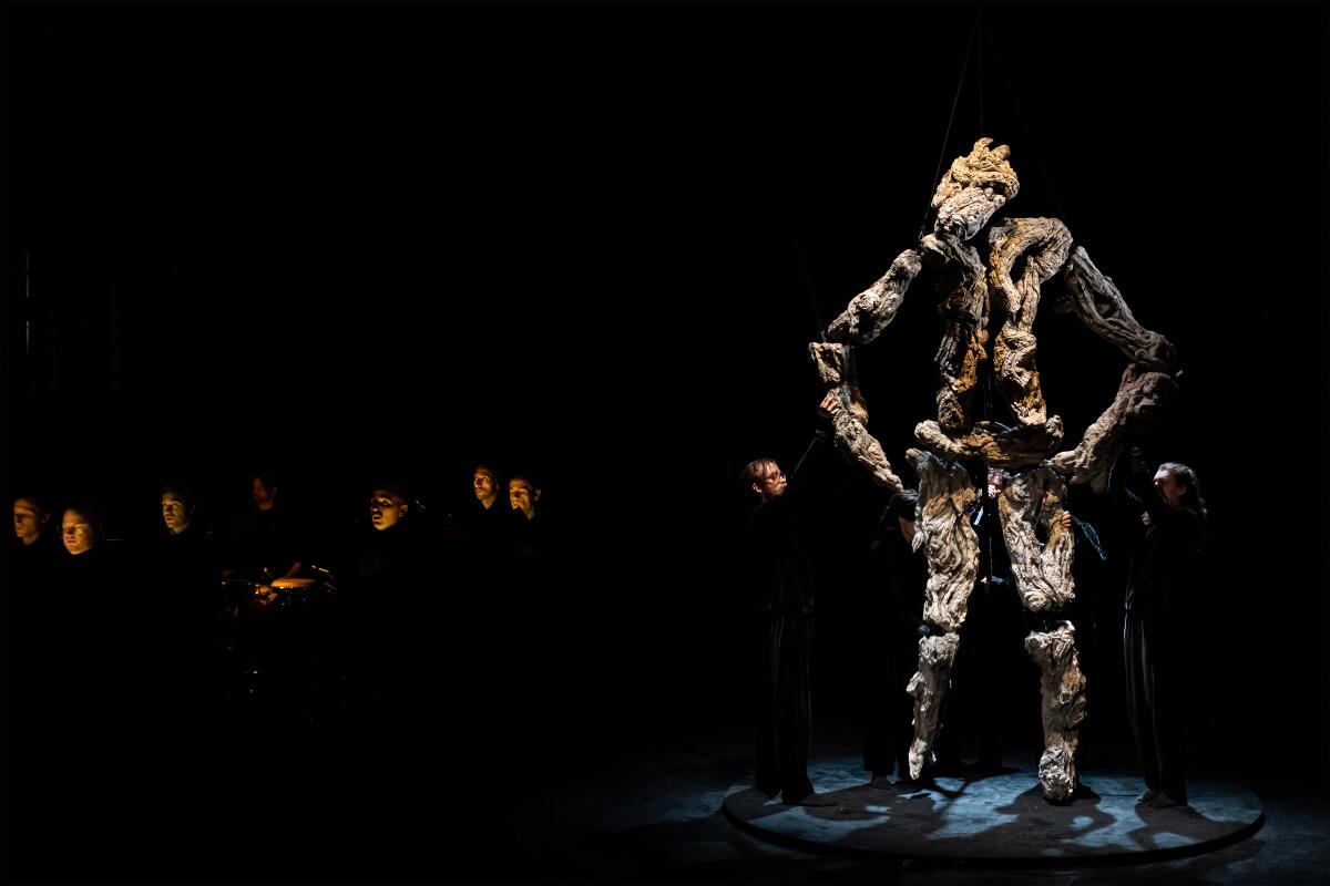 A large spotlighted puppet stands onstage with choral singers in "Book of Mountains and Seas."