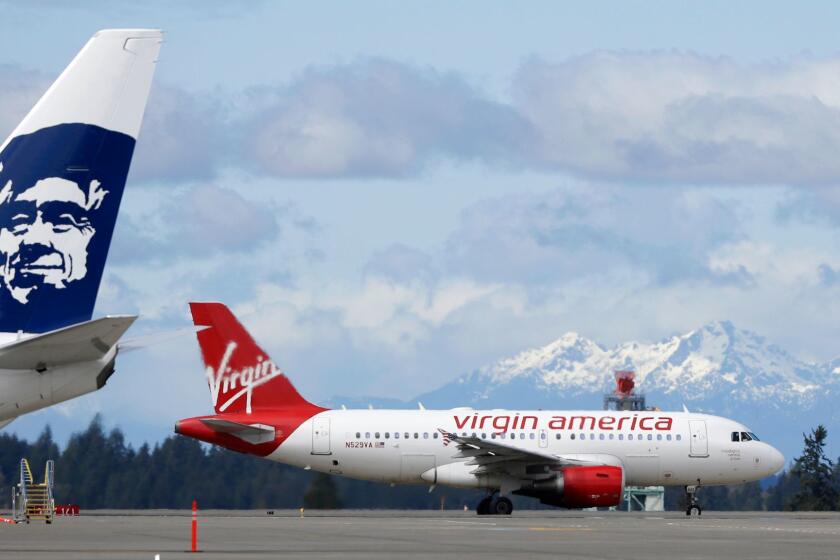 A Virgin America plane taxis past an Alaska Airlines plane waiting at a gate, Monday, April 4, 2016, at Seattle-Tacoma International Airport in Seattle. Alaska Airlines' parent company announced Monday that it will pay $2.6 billion to buy the Richard Branson-inspired, California-based Virgin America. (AP Photo/Ted S. Warren)