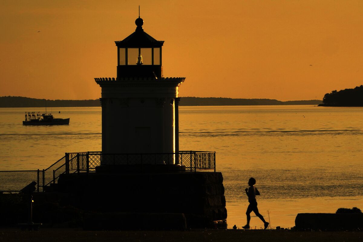 A jogger runs towards Bug Light while a lobster boat heads out of Portland Harbor under calm conditions, Tuesday morning. June 7, 2022, in South Portland, Maine. Southern Maine can expect a soaking rain on Wednesday. (AP Photo/Robert F. Bukaty)